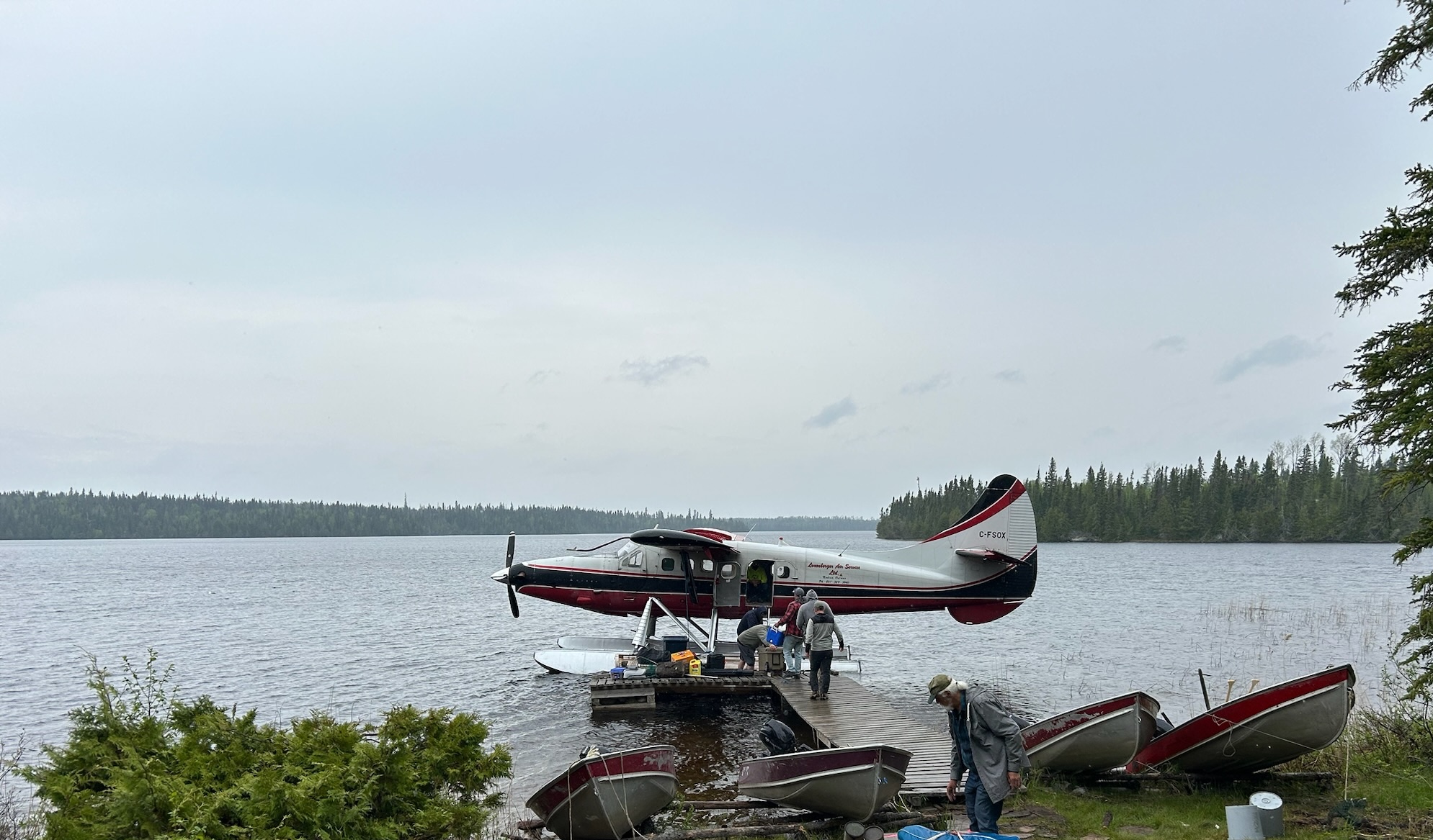 A red and white Otter floatplane docked at a wooden pier on Elbow Lake with several people loading gear.