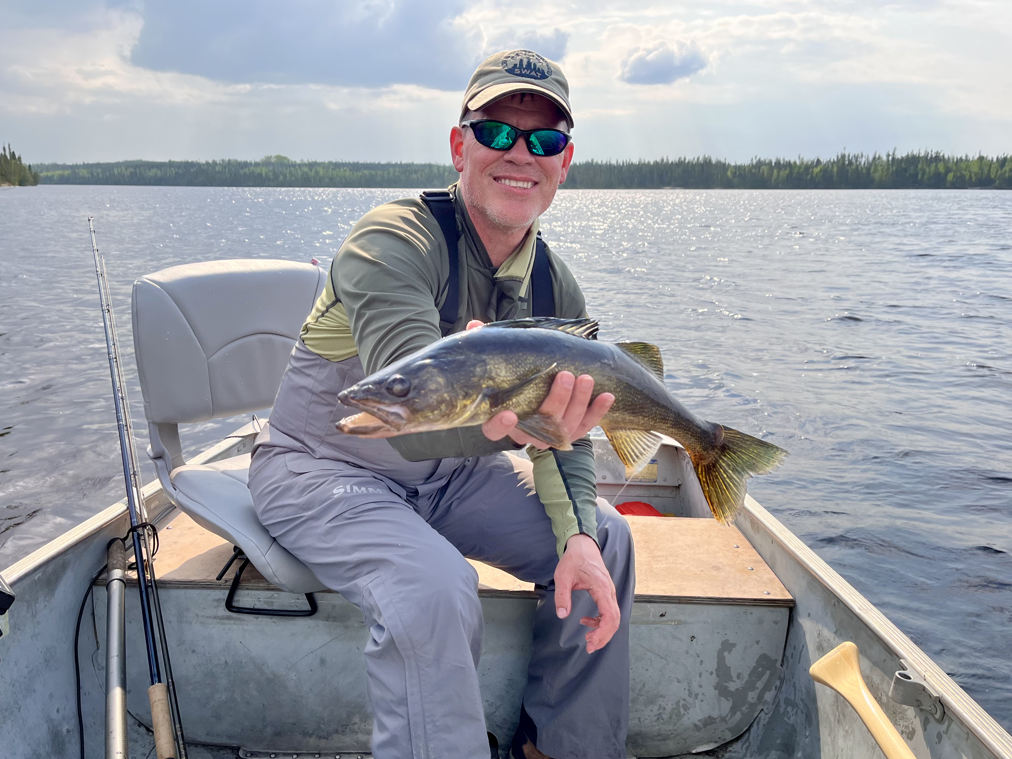 A fisherman in a boat holding a freshly caught walleye on a calm lake in the Canadian wilderness.